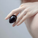 Chakrubs Xaga Yoni Egg Obsidian non-drilled held delicately between fingers, showcasing its smooth, shiny surface.