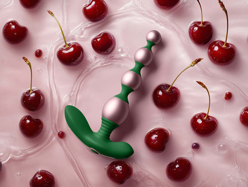 FemmeFunn Bougie Beads Rose Gold alongside fresh cherries on a pink surface, highlighting elegance and indulgence.