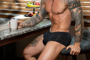 Male Power Kilauea Limited Edition Mini Short Black L showcased by a tattooed model in a modern kitchen setting.