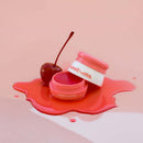 Sweetums Flavored Lip Balm Cherry with cherry on a glossy pink surface, showcasing hydration and flavor.