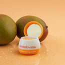 Sweetums Flavored Lip Balm Mango with mangoes on a bright surface, highlighting the product's tropical flavor.