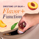 Sweetums Flavored Lip Balm Vanilla in a hand reaching for it inside a bag with peach slices and greenery.