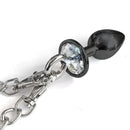 NIXIE Metal Butt Plug & Furry Handcuff Set Black featuring a shiny jewel butt plug connected by a chain.