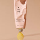 Sex Au Naturel Vulva Balm Soothing Moisturizer tube with balm oozing from the tip on a reflective surface.