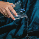 A hand pouring water from a glass onto a Splash Blanket The OG Small Emerald Green, showcasing its waterproof feature.