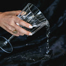 Pouring water from a glass onto the Splash Blanket The OG Large Waterproof Black, showcasing its waterproof feature.