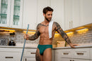 Male Power Ripple Moon Jock Teal S/M showcased by a man in a modern kitchen, featuring a bold design and supportive fit.