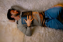 Male Power Eco Cozy Cutout Thong Green S/M on a relaxed man reading a book while lying on a fluffy surface.