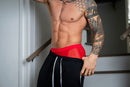 Male Power Mesh 2.0 Mini Short Red S showcased on a muscular man with tattoos in a stylish indoor setting.