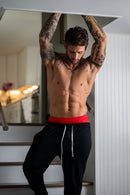 A man showcasing Male Power Mesh 2.0 Mini Short Red Large with tattoos and stylish black pants.