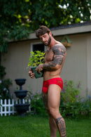 Male Power Sassy Lace Bikini Solid Pouch Navy XL model holding plants outdoors in red lace bikini.