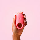 Ily By Je Joue Vibrating Cock Ring held in a hand against a pink background.