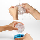 Hands demonstrating the Tenga Geo Glacier Textured Male Masturbator in use with water.