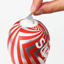 Hand peeling back the top seal of the Super Tenga Meteor Smash Masturbator for easy access.