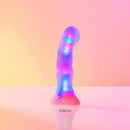 Love To Love Sugar Bomb LED Silicone Dildo glowing in vibrant colors against a pink background.