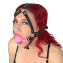 Ple'sur Face Harness Ball Gag Pink worn by a model featuring a pink ball gag and black harness straps.