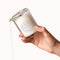 Dame Massage Oil Candle Melt Together held in hand, melting oil pouring from the jar, showcasing its luxurious design.