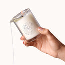 Dame Massage Oil Candle Soft Touch being poured from a glass container with a lit wick and melting wax.