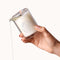 Dame Massage Oil Candle Soft Touch being poured from a glass container with a lit wick and melting wax.