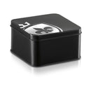 Mystim Pearly Pete Corona Glans Strap packaging in a sleek black tin with a decorative emblem on top.