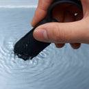 A hand holding the Tenga SVR Smart Vibe Ring Black as it creates ripples in water.