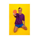 Cute Little Fuckers Starsi Palm Vibrator Coral held by a smiling person in colorful attire against a vibrant yellow background.