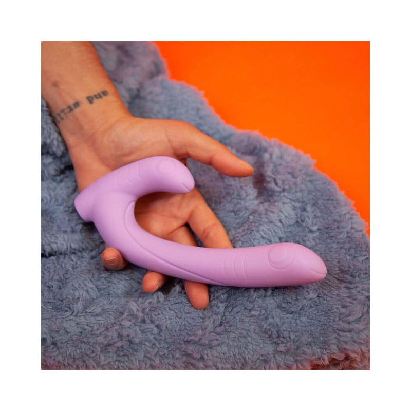 Cute Little Fuckers Jix Vibrator Lavender held in hand on fluffy blue surface.