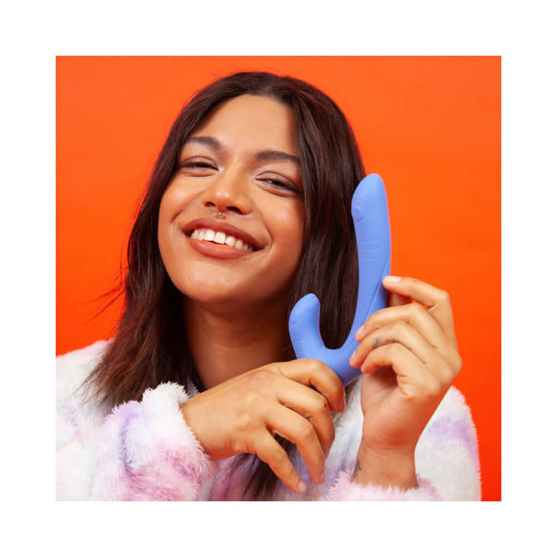 Cute Little Fuckers Jix Vibrator Periwinkle held by a smiling woman against an orange background.