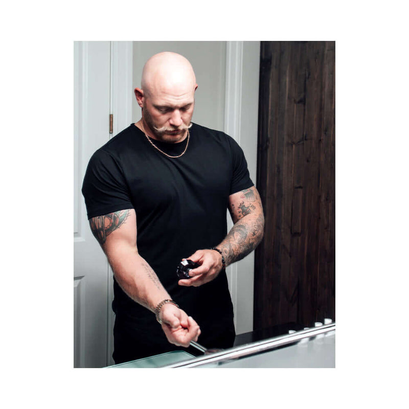 Man applying Eye of Love Matchmaker Black Diamond Attract Her Parfum 1 Oz in front of a bathroom mirror.