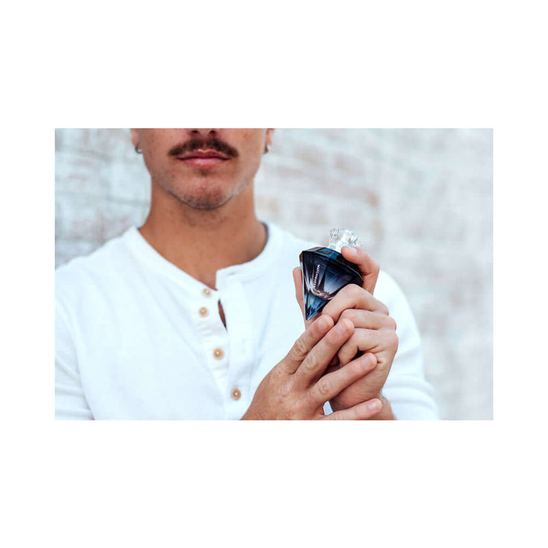 A man holding Eye of Love Matchmaker Black Diamond Attract Him Parfum 1 Oz confidently with a stylish look.