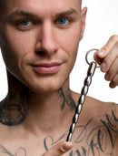 Master Series Mortal Coil Stainless Steel Urethral Sound held by a tattooed male model, showcasing its sleek design.