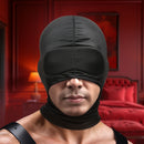 Master Series Cocksucker Blindfold Hood Black worn by a model in a stylish red room, enhancing sensory deprivation.