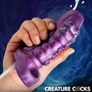Tentacle Squirting Silicone Penis Enhancer Purple held in a hand against a swirling blue background.