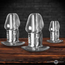 Master Series Dicked Clear Hollow Anal Plug 3 Piece Set displayed on a wooden surface.