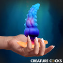 Glowtopus Glow-in-the-Dark Silicone Anal Plug held in a hand against a blue background, showcasing its unique tentacle design.