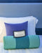 Luxurious bedding with purple and teal pillows and a decorative sign on a neatly made bed.