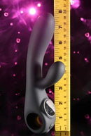 Black Magic Rechargeable Silicone Rabbit Vibrator standing next to a ruler for size reference against a pink backdrop.