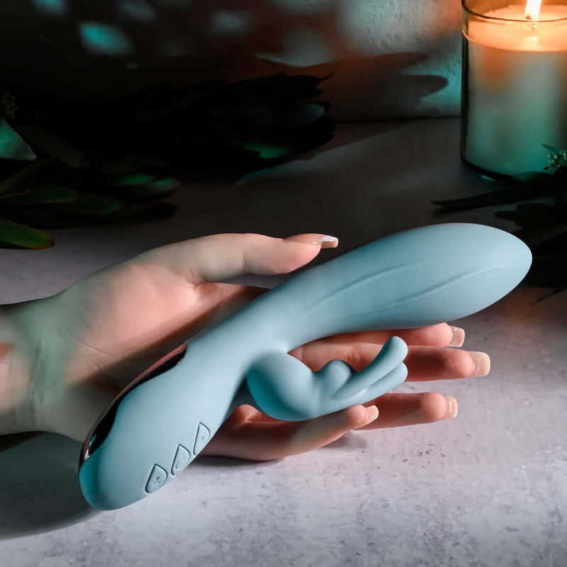 Hand holding the EVOLVED BOSS BUNNY Silicone Rabbit Vibrator with a candle lit background.