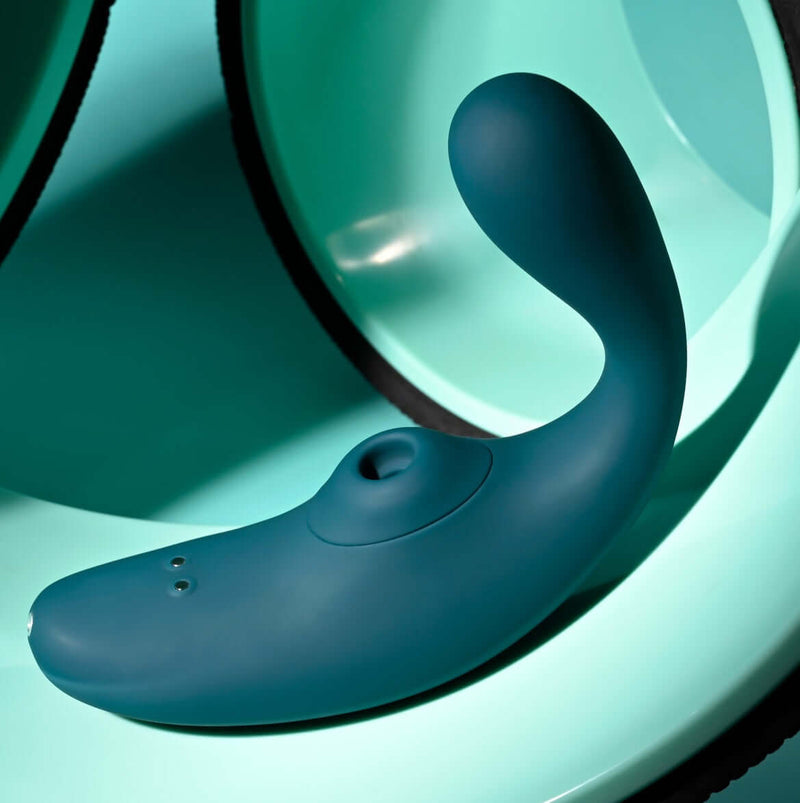 Playboy Charmer dual vibrator with clitoral suction in teal green, waterproof and rechargeable, displayed on mint green background.