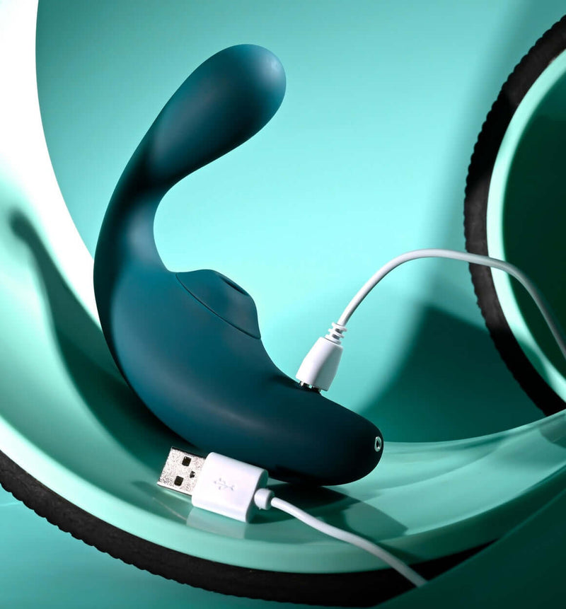 Playboy Charmer dual vibrator with clitoral suction and flexible shaft, shown charging with USB cable, waterproof and rechargeable design.