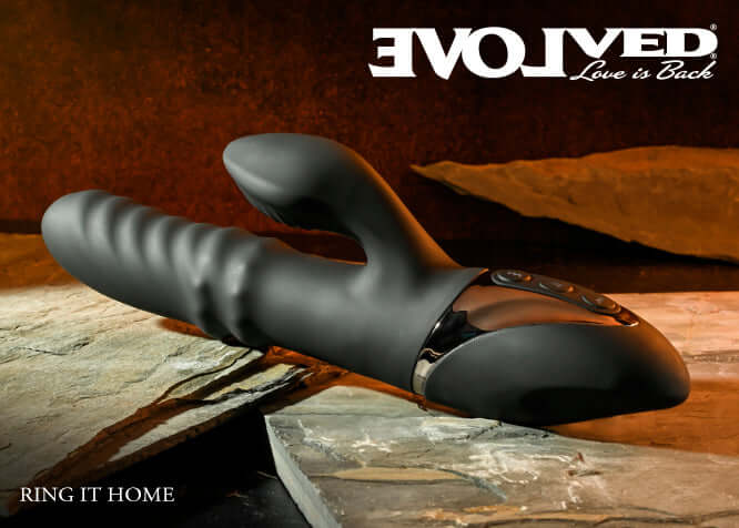 Evolved Ring It Home Silicone Rechargeable Vibrator with dual clitoral stimulator in black on textured surface.