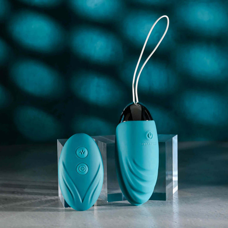 Evolved Oval Office Remote Control Vibrating Egg in turquoise placed on a glass platform with remote control adjacent