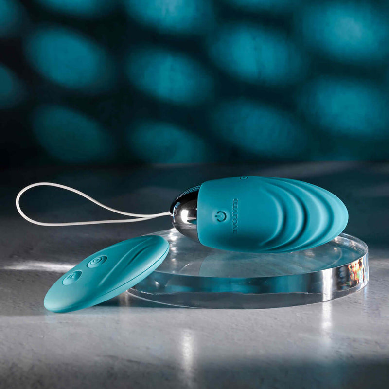 Evolved Oval Office remote control vibrating egg in teal color, shown on a clear stand with matching remote control, ideal for discreet pleasure.