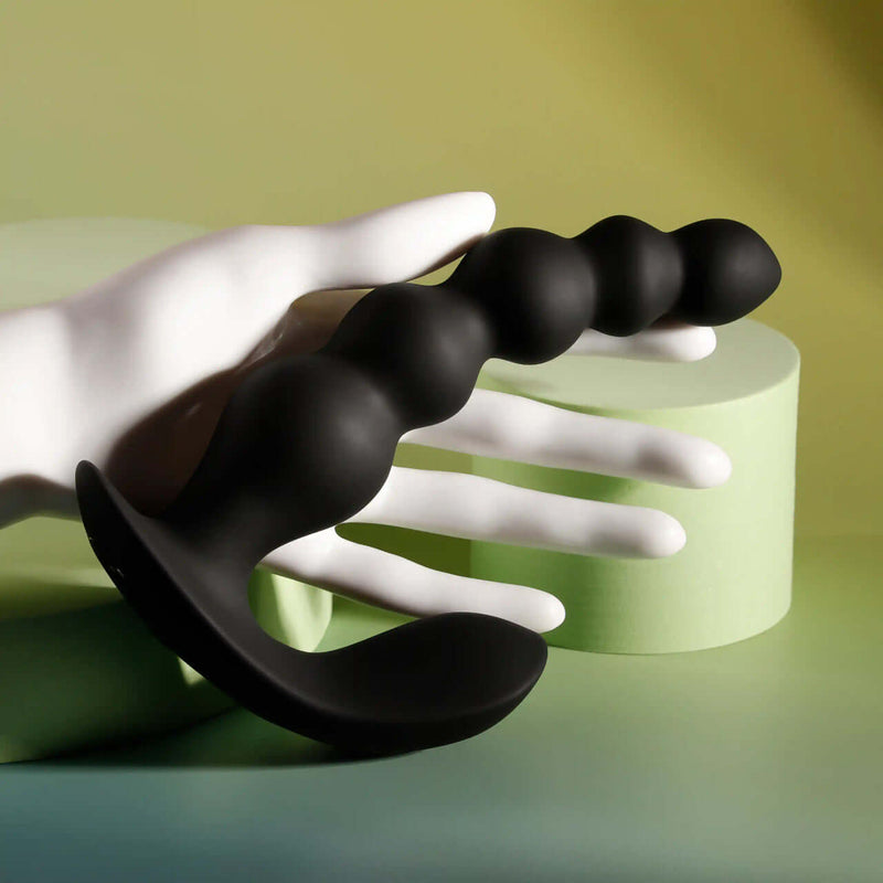 Black silicone vibrating anal beads held in a hand, featuring graduated sizes and a curved design for intimate stimulation.