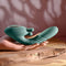 Green poseable thrusting vibrator with rotating prongs, textured shaft held on a wooden surface against a neutral background.