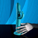Blue rechargeable silicone rabbit vibrator with thrusting feature and suction cup base on a reflective surface.