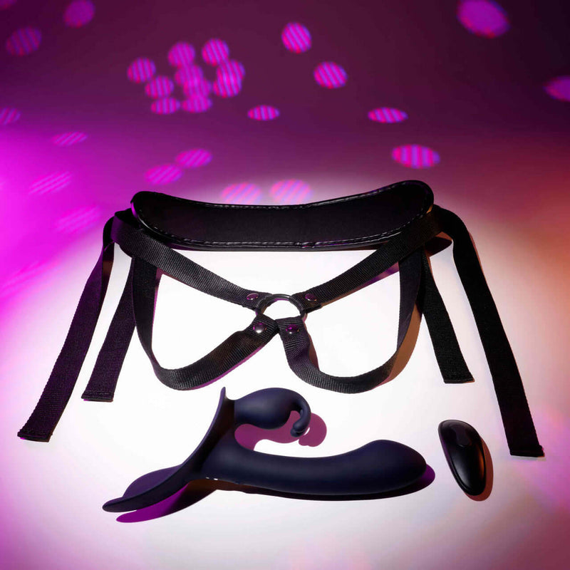 Giving Vibes Rechargeable Silicone Triple Vibrator in purple with adjustable harness and remote, on a vibrant background.