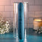 Queen of All Trades blue silicone dual vibrator displayed in a glass container surrounded by candles and flowers.