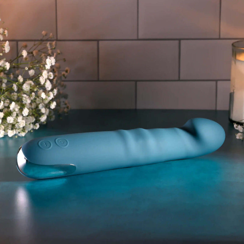 Rechargeable blue silicone dual vibrator on a table with flowers, designed for intense pleasure and satisfaction.