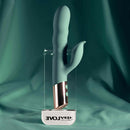 The Shimmy Vibrator with Clitoral Stimulator Green displayed on a clear stand against a teal background.
